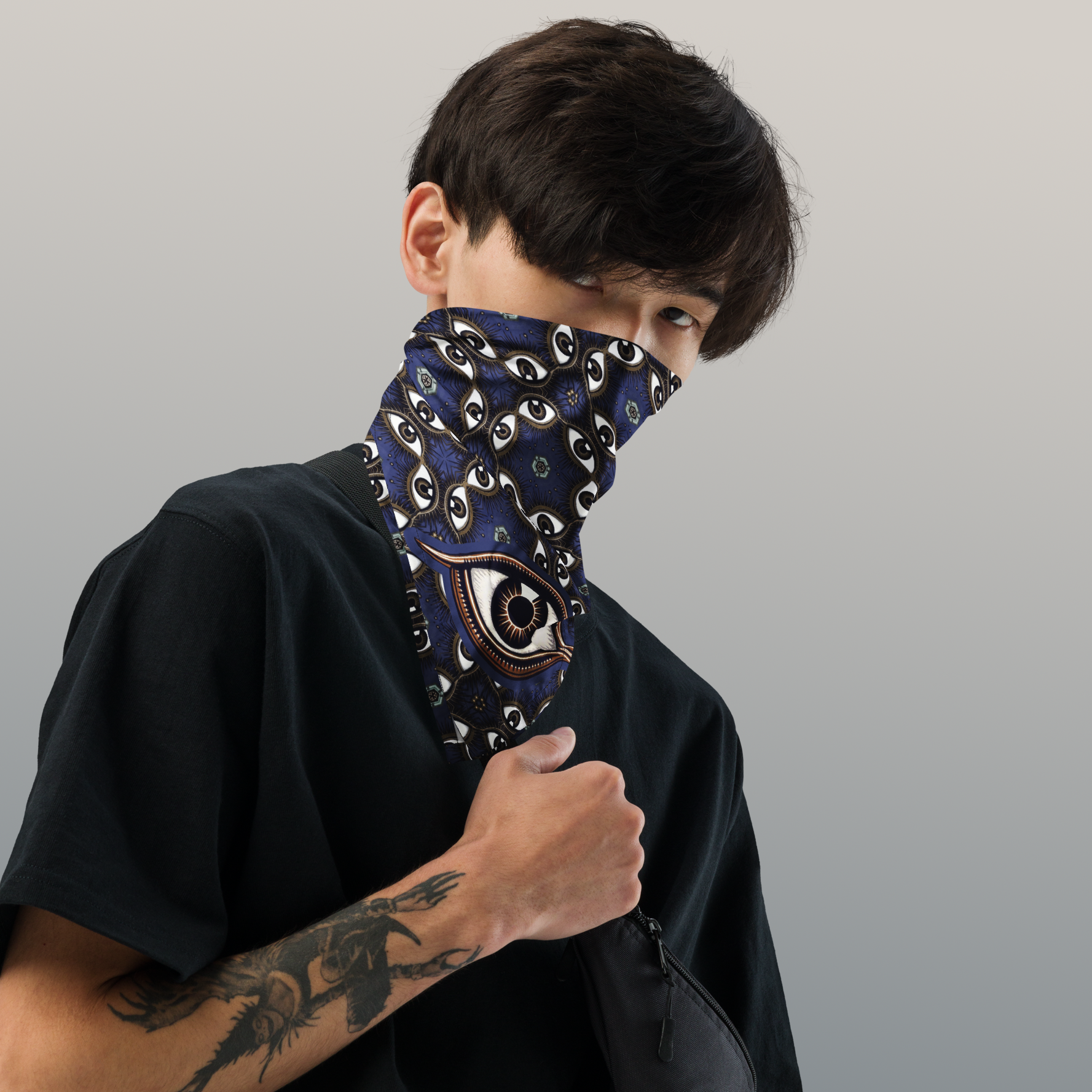 Made for the bold, a deep blue bandana with aal-seeing eye pattern, black, white and tan accents, worn as a gaiter by handsome young man. 